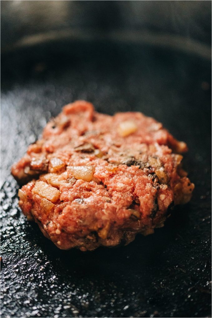 A Shields Valley Ranchers ground beef hamburger patty sizzles in a cast iron pan.