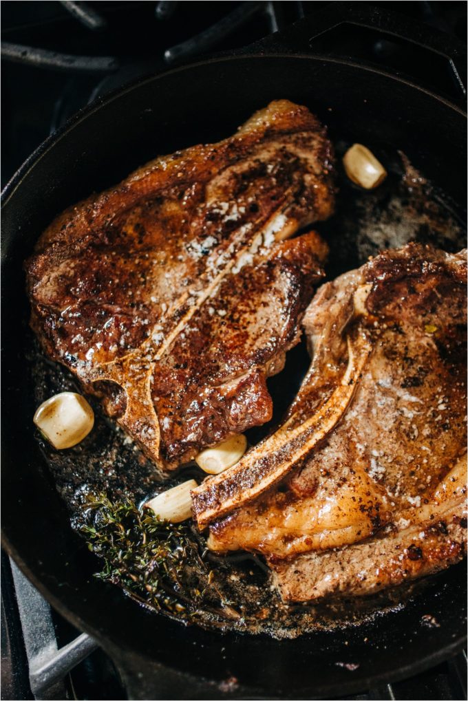 Shields Valley Ranchers rib and T-bone steaks topped with pats of butter brown nicely alongside thyme sprigs in a cast iron pan for perfect pan-seared steak on the stove.
